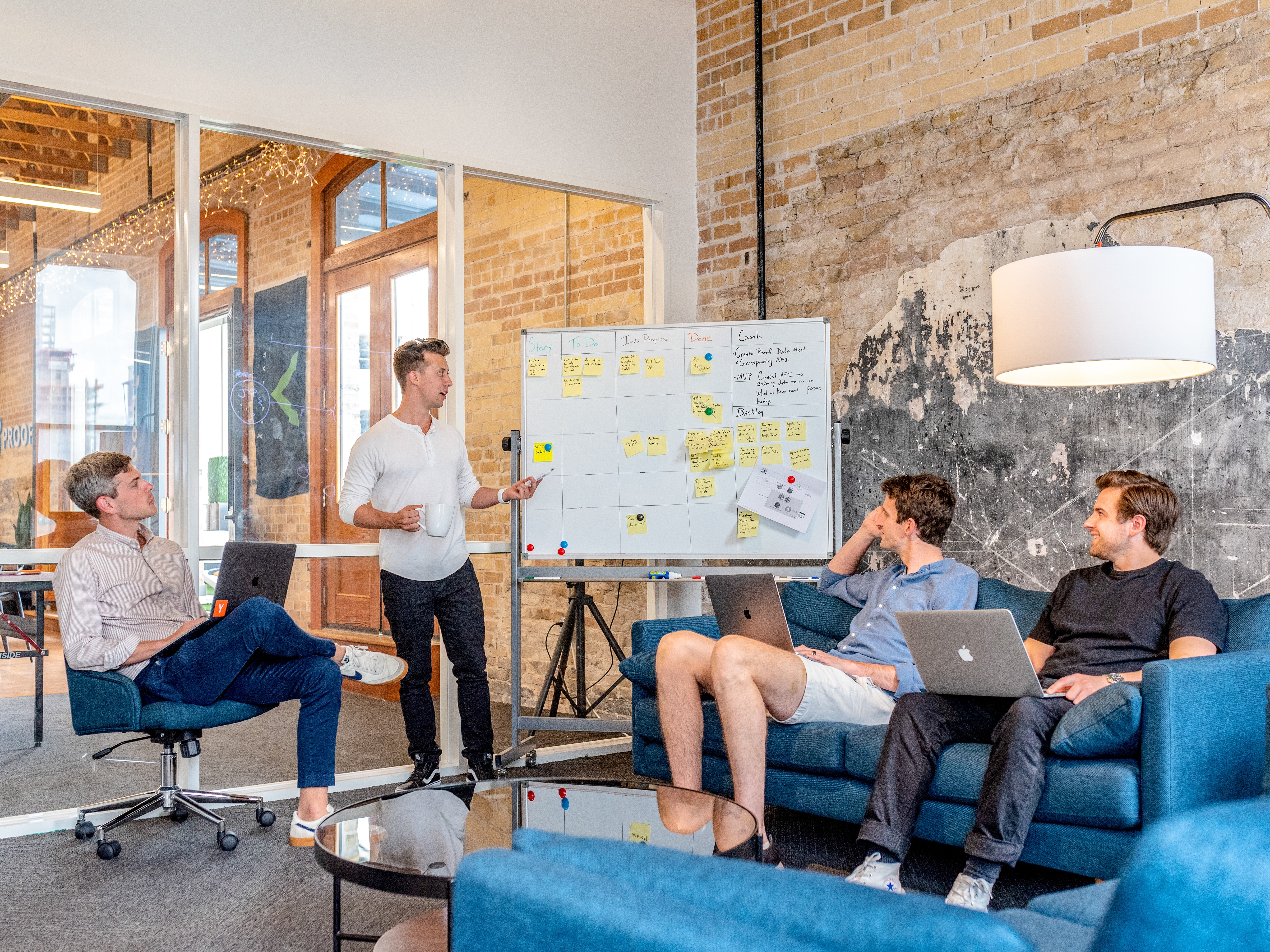 4 people discussing something with post it notes on whiteboard and laptops