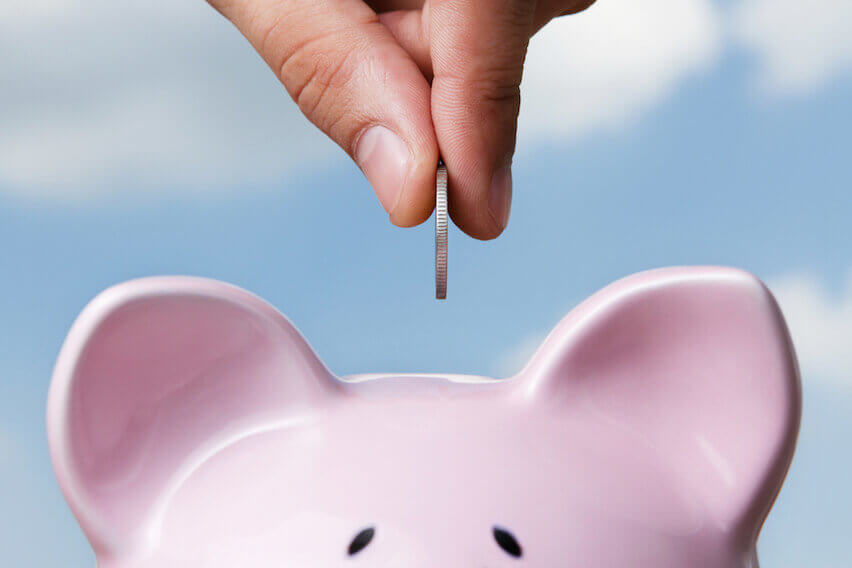 Hand putting a coin into a pink piggy bank