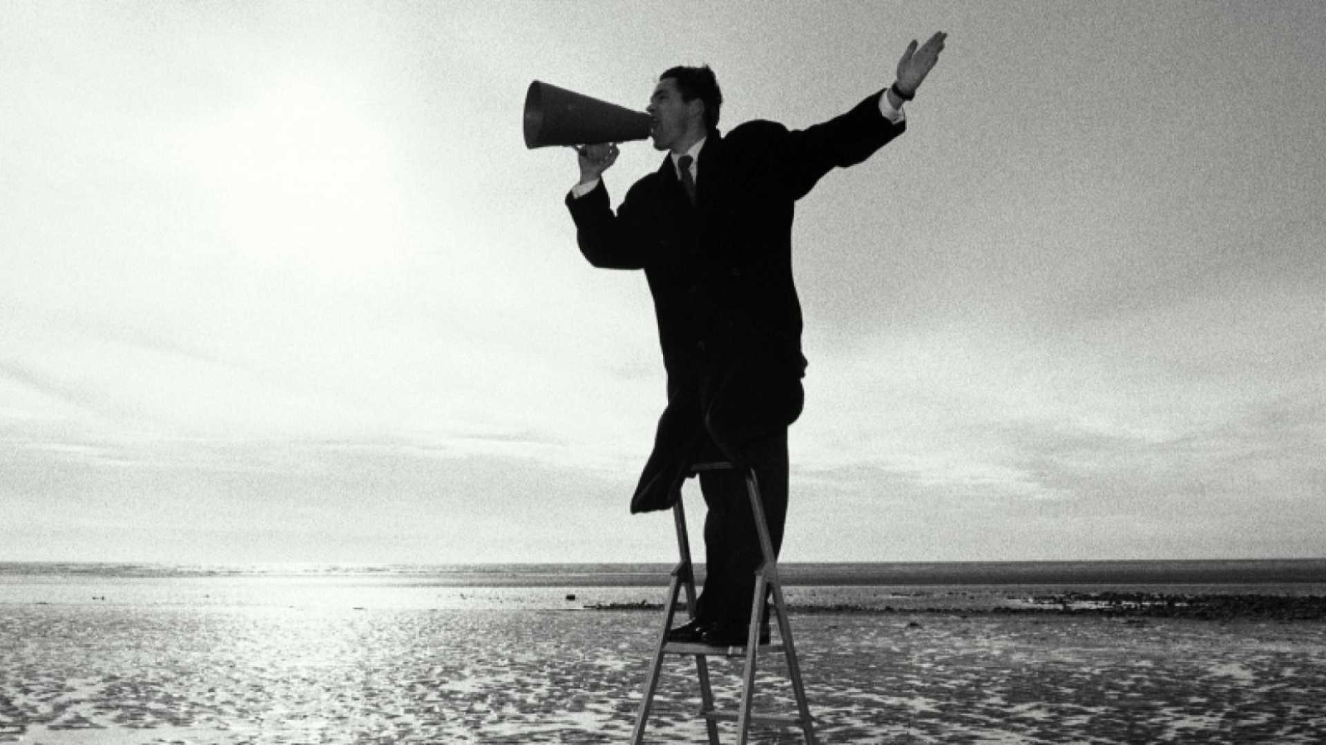 A man holding a megaphone while standing on a staircase ladder leveller