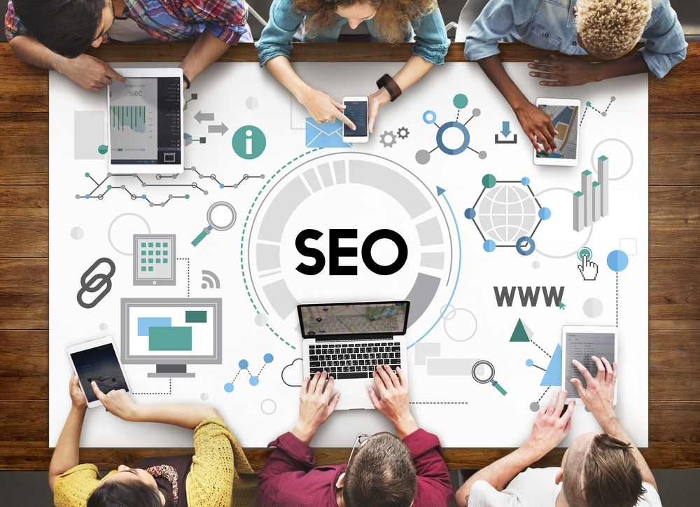 A group of people discussing SEO holding their smartphone and Laptop on a tech-decorated table