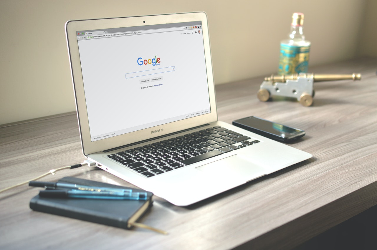 Google in laptop with phone, small notebook and pens beside it