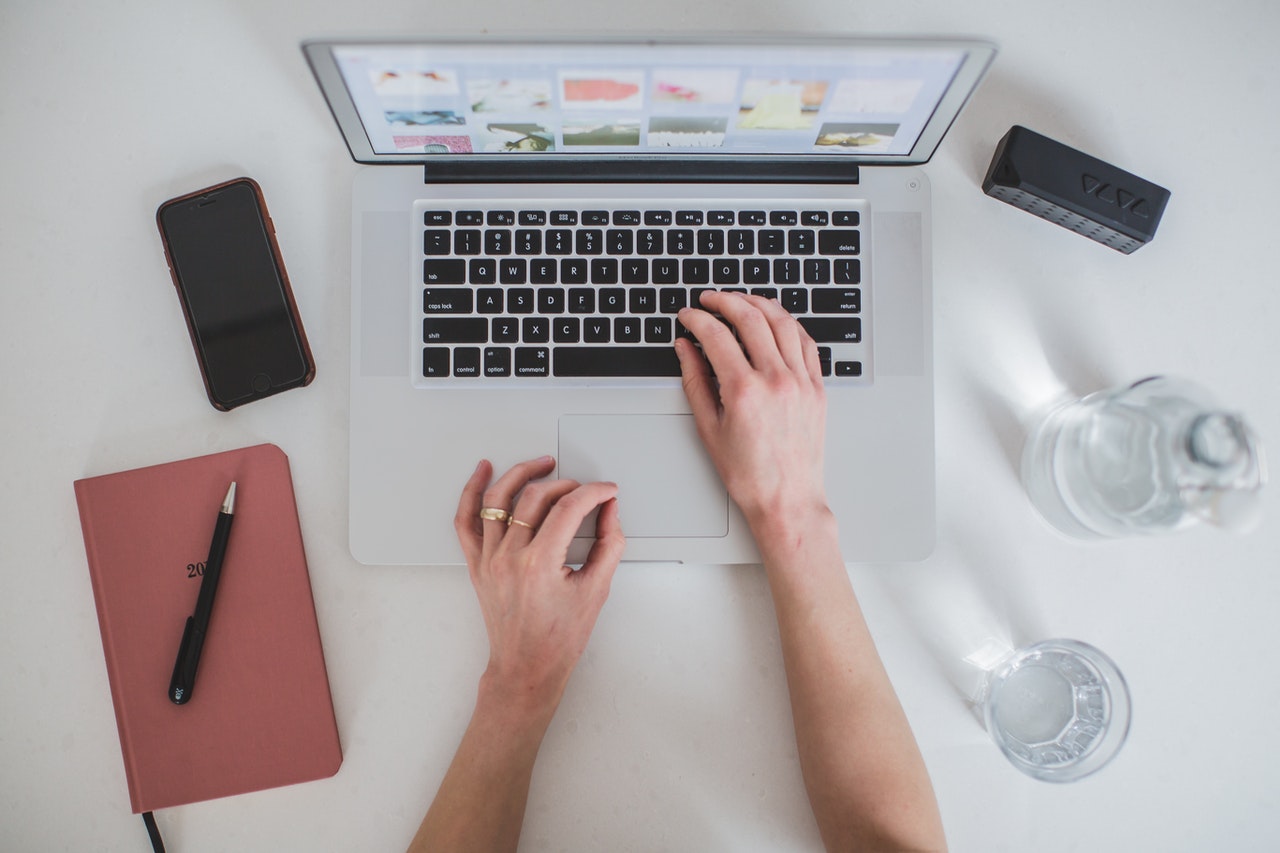 A hand using keyboard, with notebook, phone, and glass of water beside