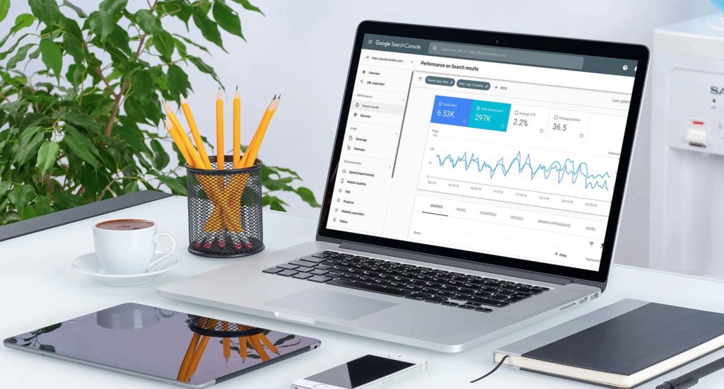 Laptop with google statistics and notebook, pencil and pencil holder beside it and a phone in front of it