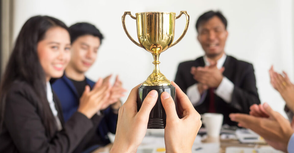 A hand holding a trophy and people on surrounding clapping