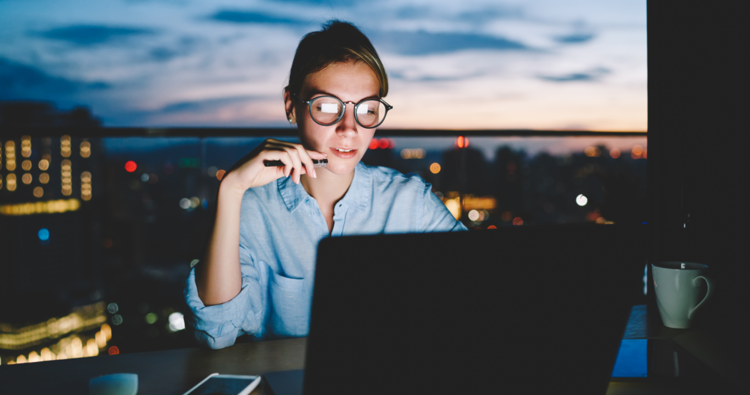 A girl wearing eyeglasses looking at a laptop with a pen in her hand