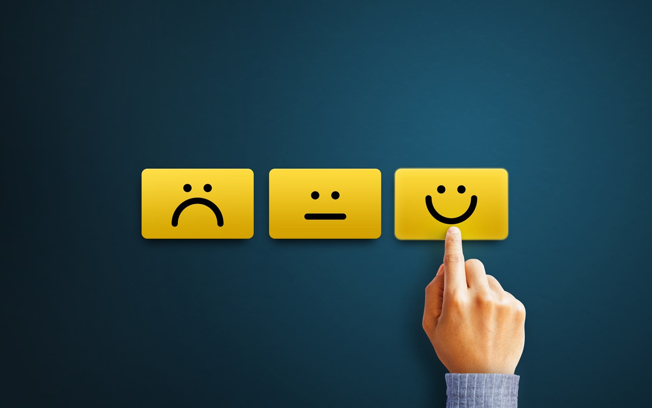 A hand pressing a happy face and poker face, and sad face beside it