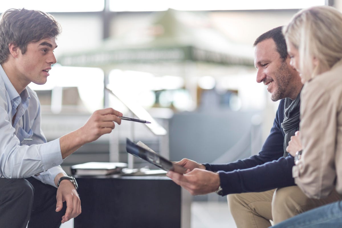 A man and a woman looking in a paper and a man in front of them talking