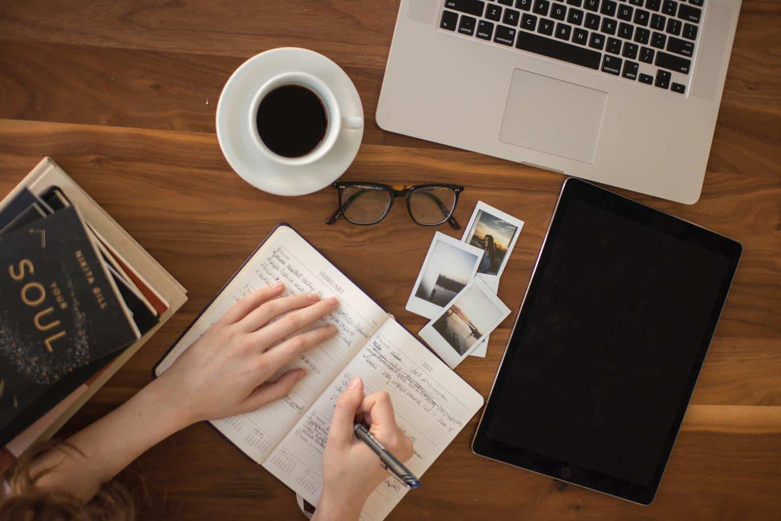 A woman writing in a notebook with tablet and pictures beside it