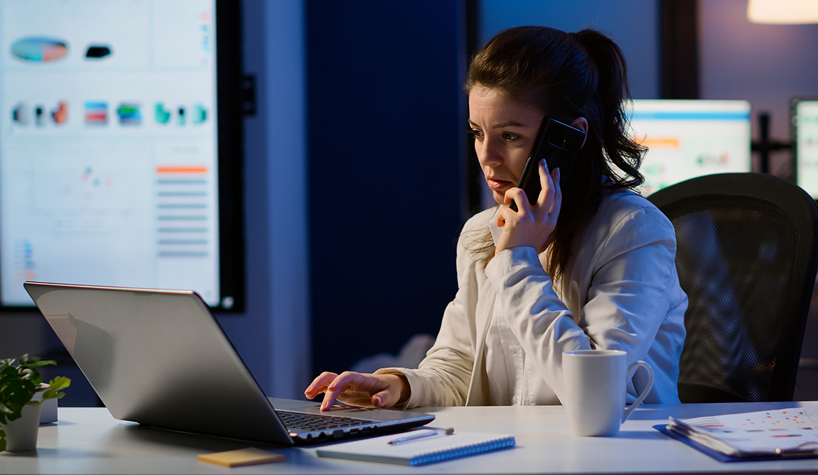 A female account manager speaking on her cell phone while seated in front of her laptop at her desk