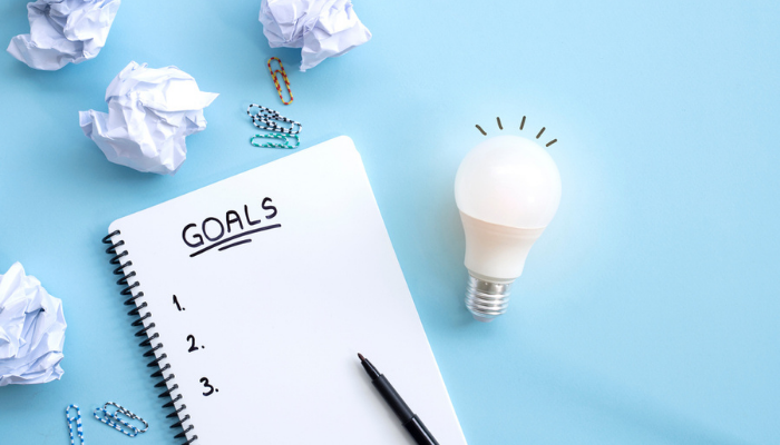 A notebook labeled "Goals" and a pen next to a light bulb and crumpled papers