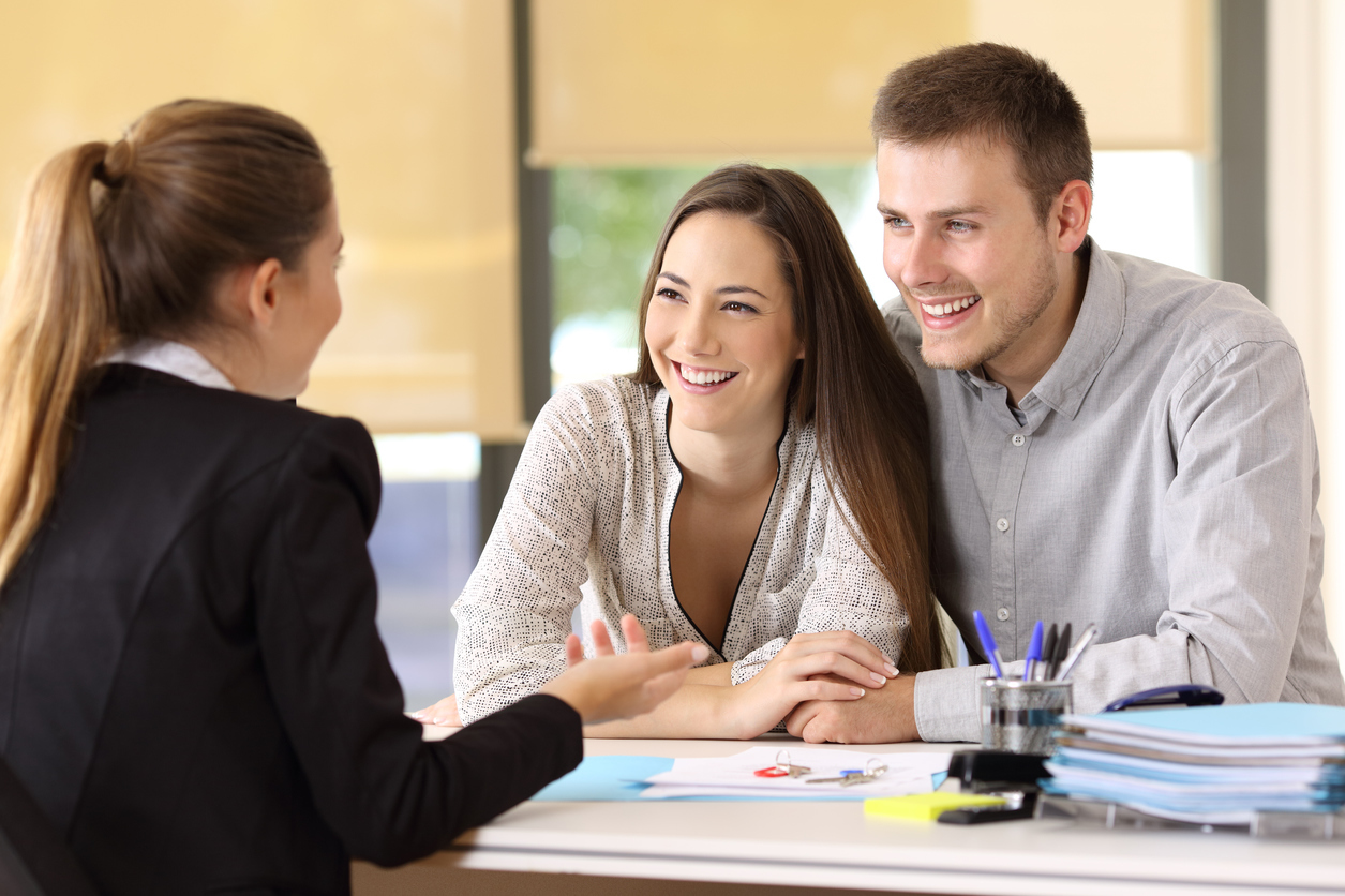 A couple and a grl in suit talking with papers and pens on the table