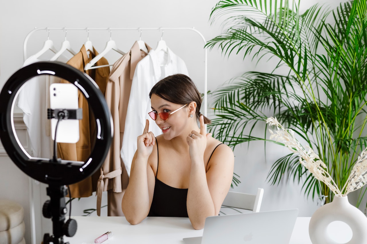 A female micro influencer vlogging in her room, with clothes hanging on a rack and a green plant in one corner