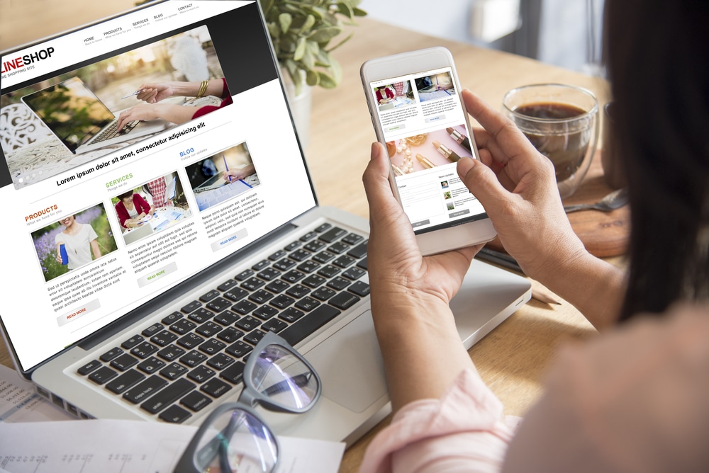 A woman's cellphone in front of a laptop with the same website
