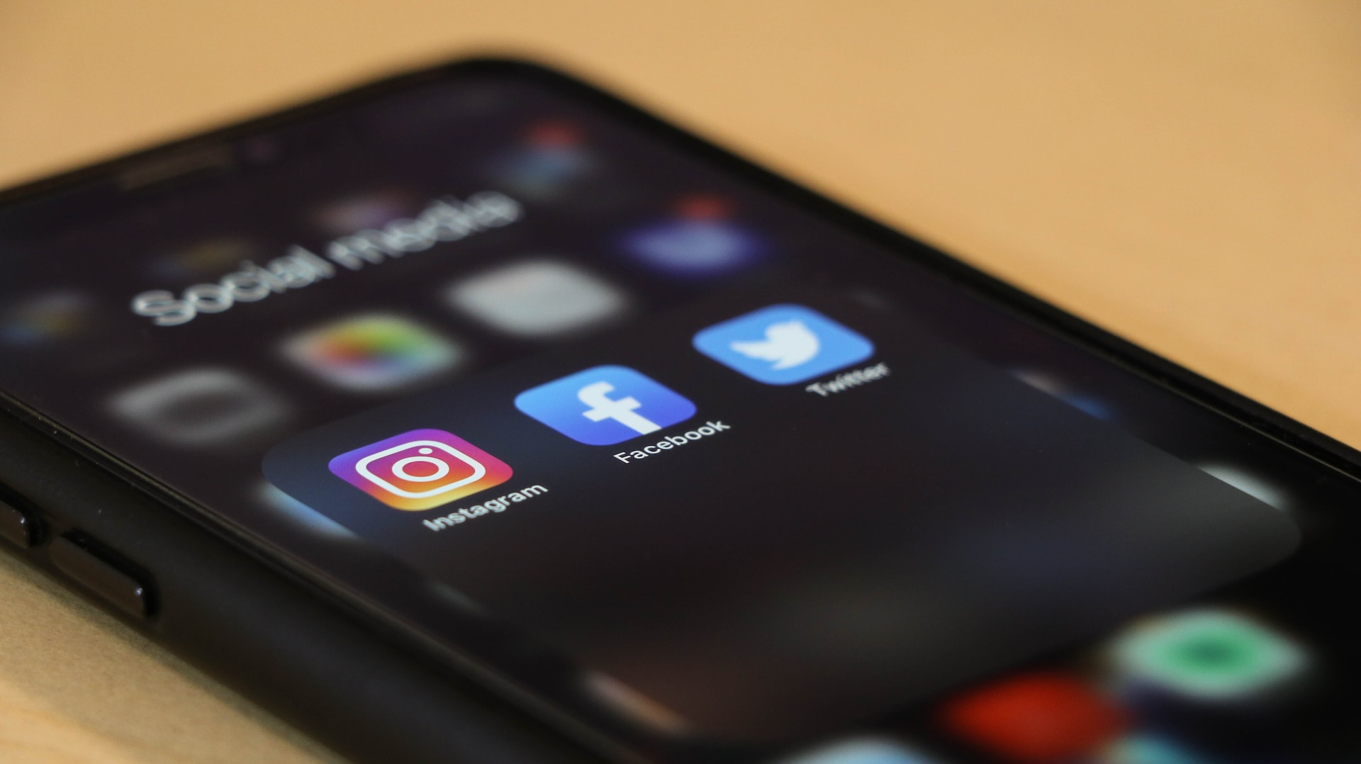 A black smartphone lying on a surface, with screen showing the app icons of Instagram, Facebook and Twitter