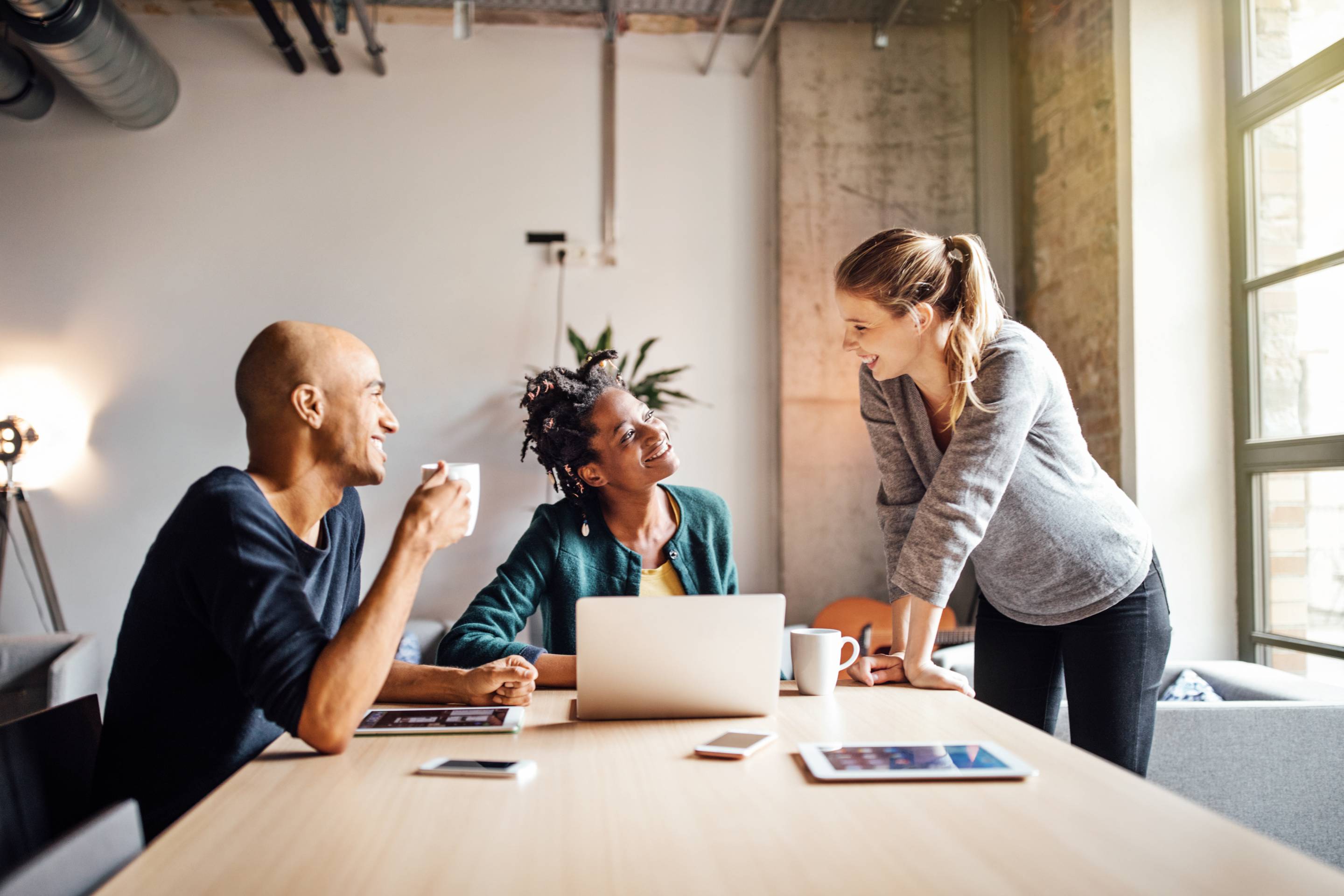 Two girls and a man smiling while talking and a laptop in front of them