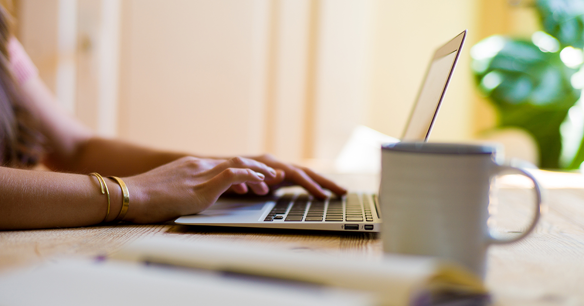 A woman typing in a laptop with a mug on the side