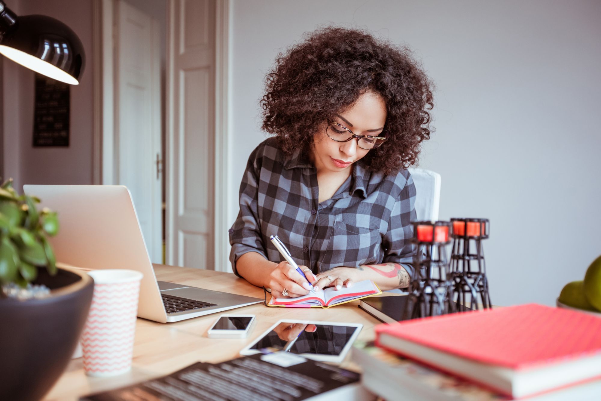 A woman writing on a notebook with laptop in front of her