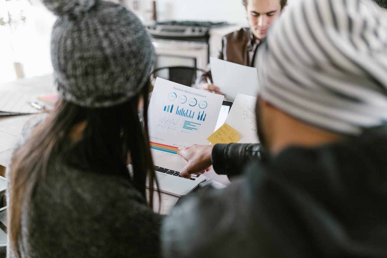 A male and female marketers wearing beanies looking at business metrics presented in colorful bar graphs