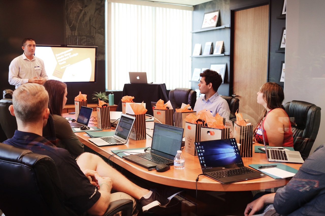 A male team leader discusses B2B case studies with his seated male and female members with their laptops
