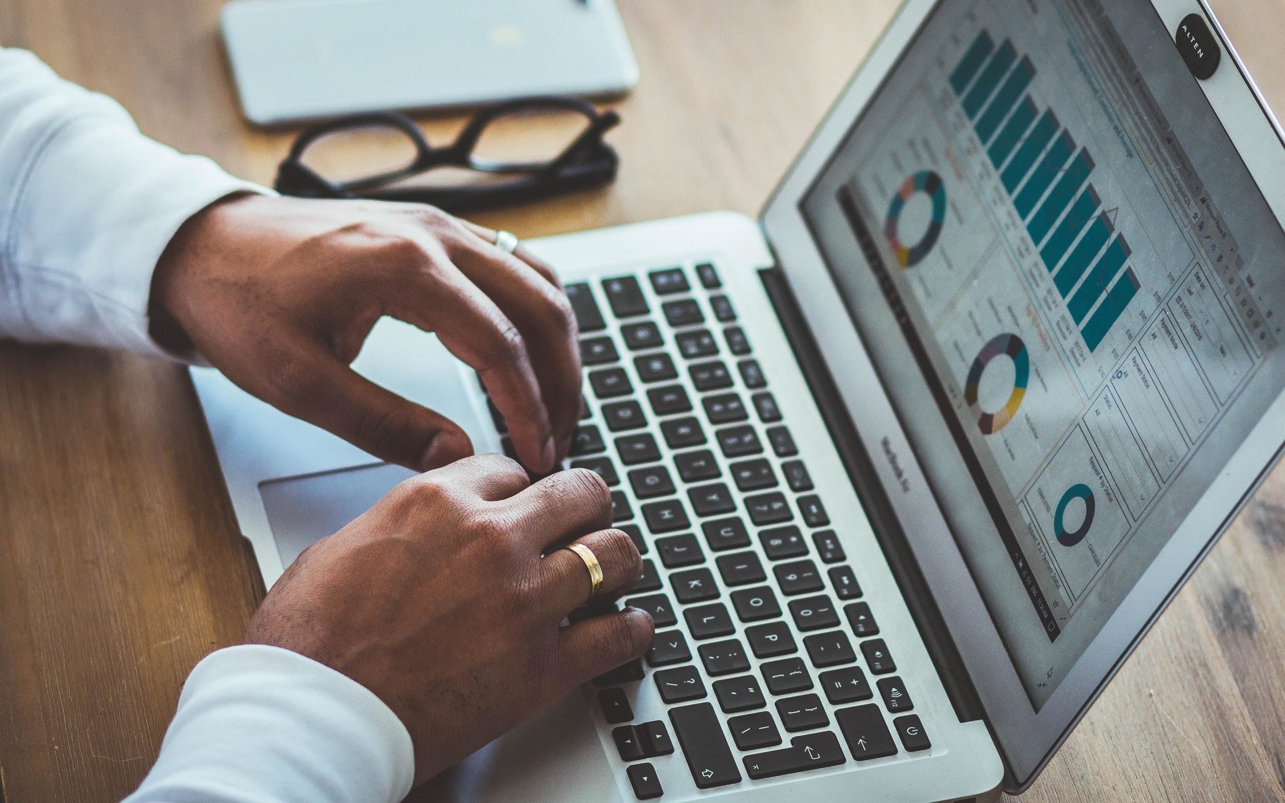 Hands typing on a laptop with graphs