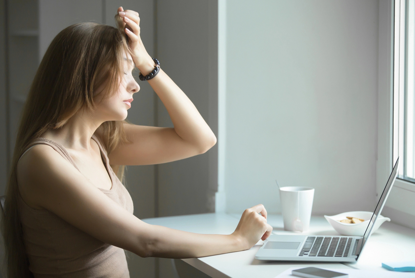 A giirl holding her forehead while looking at the laptop in front of her