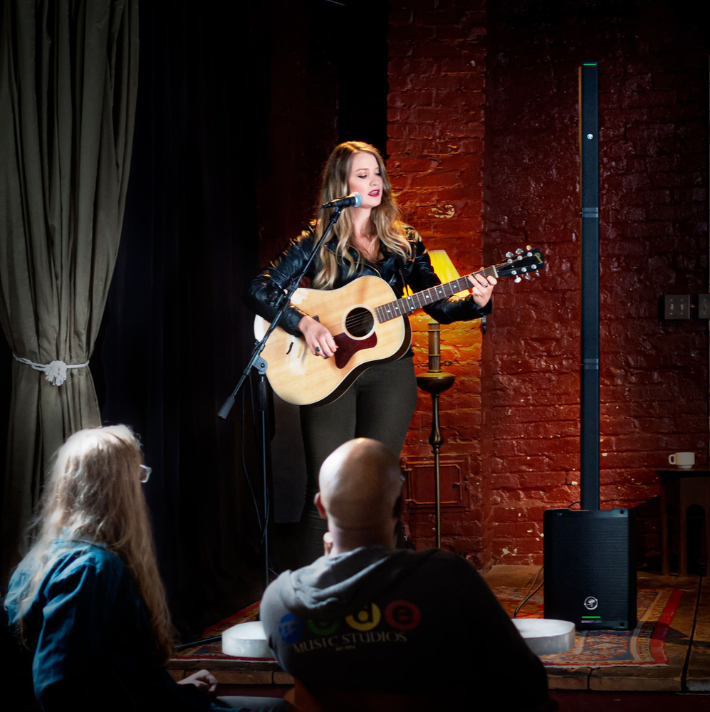 Girl on stage with a guitar on Open Mic Nights