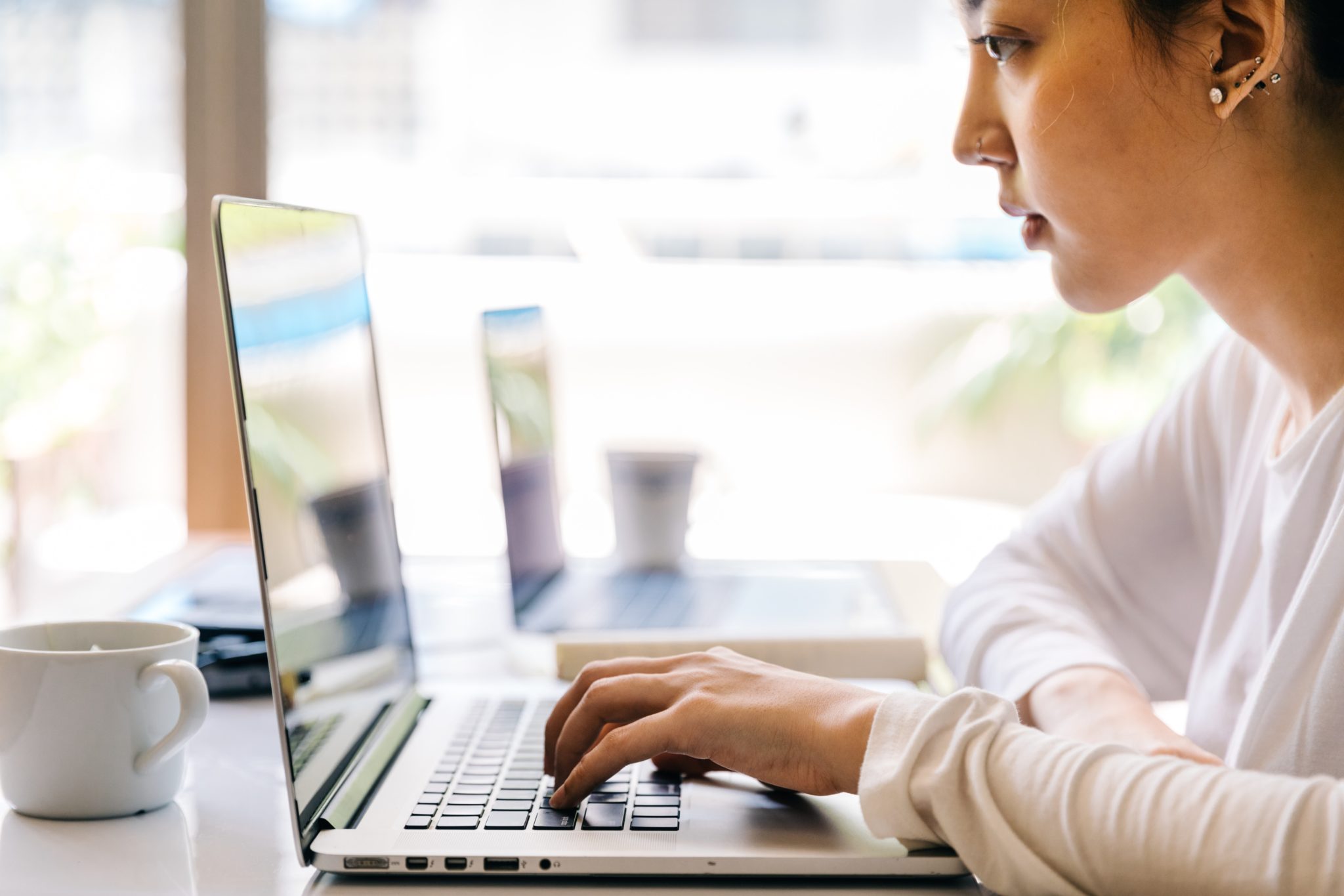 A woman in beige cardigan typing on a laptop