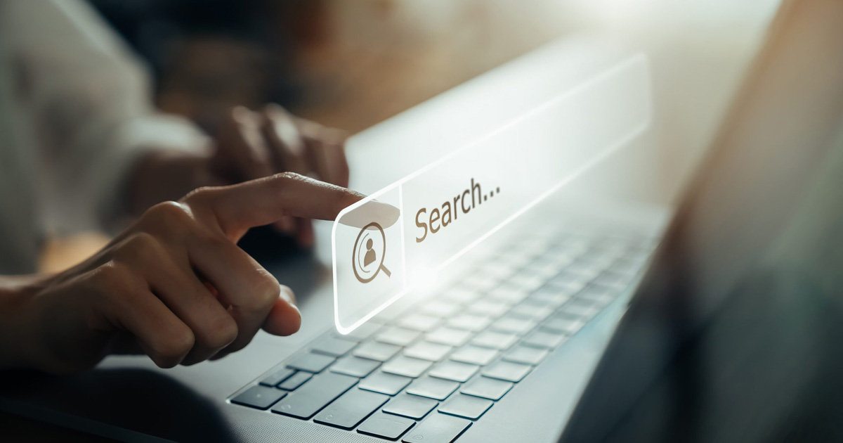 A hand touching a floating search bar and a laptop