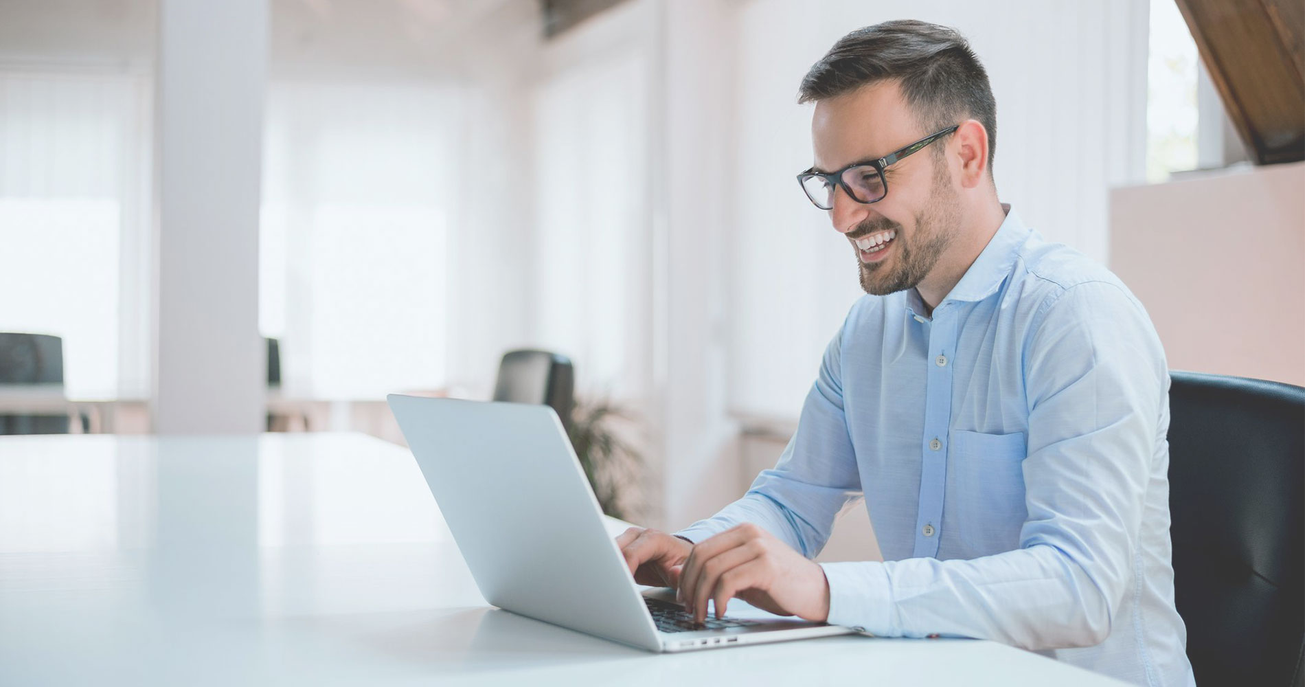 A man in light blue polo long sleeves typing on a laptop in front of him