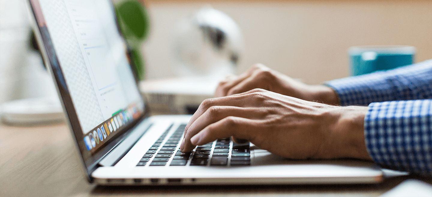 A person in blue checkered long sleeves typing on laptop