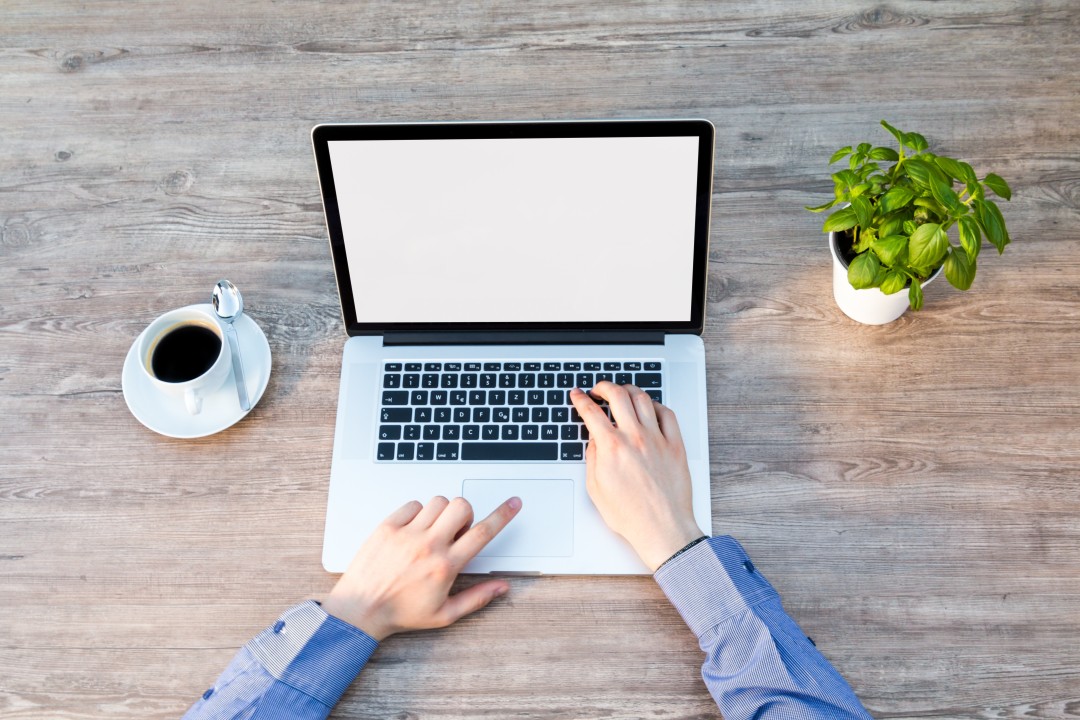 Hands typing on a laptop with coffee beside it