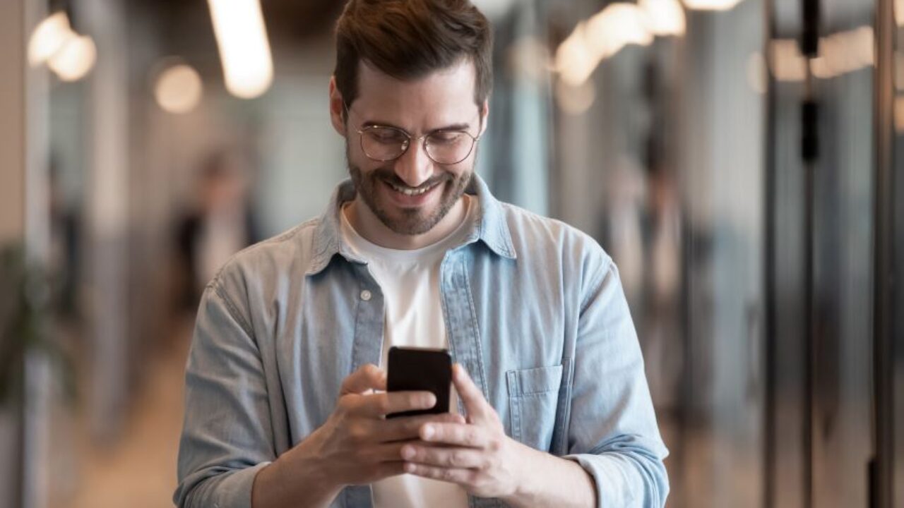 A man wearing a light blue polo long sleeves holding a phone
