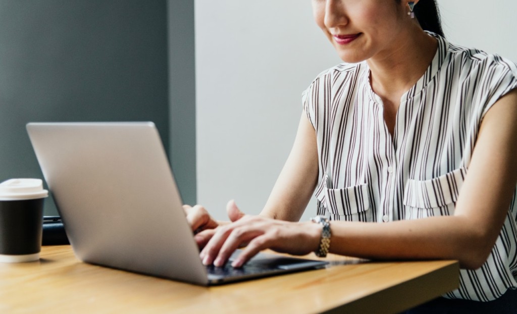 A woman in white stripes top typing on a laptop