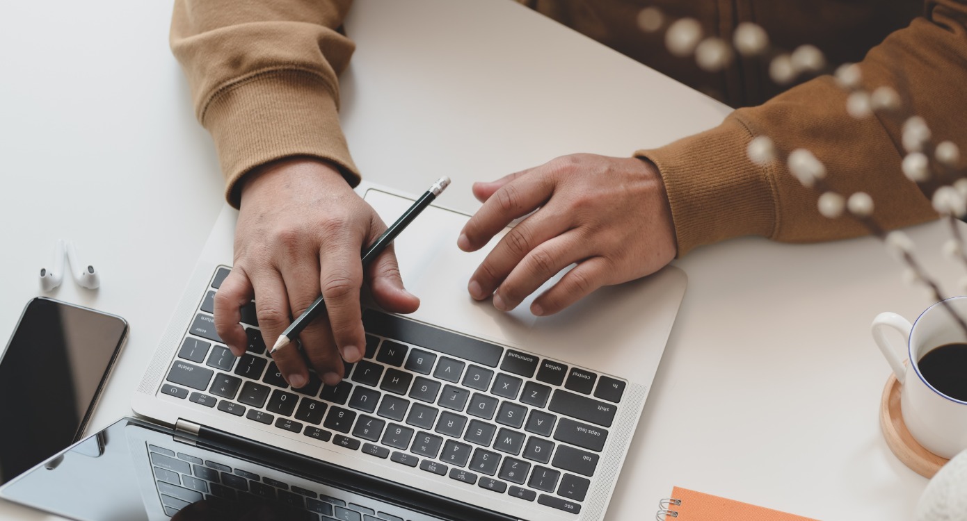 A woman typing on a laptop while holding a pencil