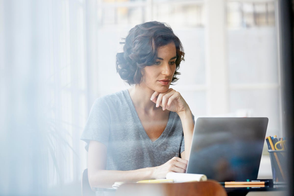A woman in gray shirt looking at her laptop
