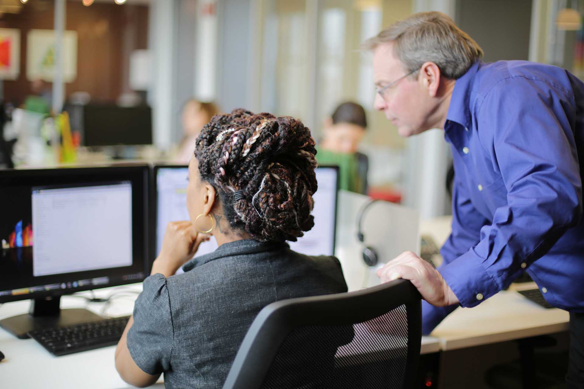 A woman in gray shirt and a man in blue long sleeves looking at a computer monitor