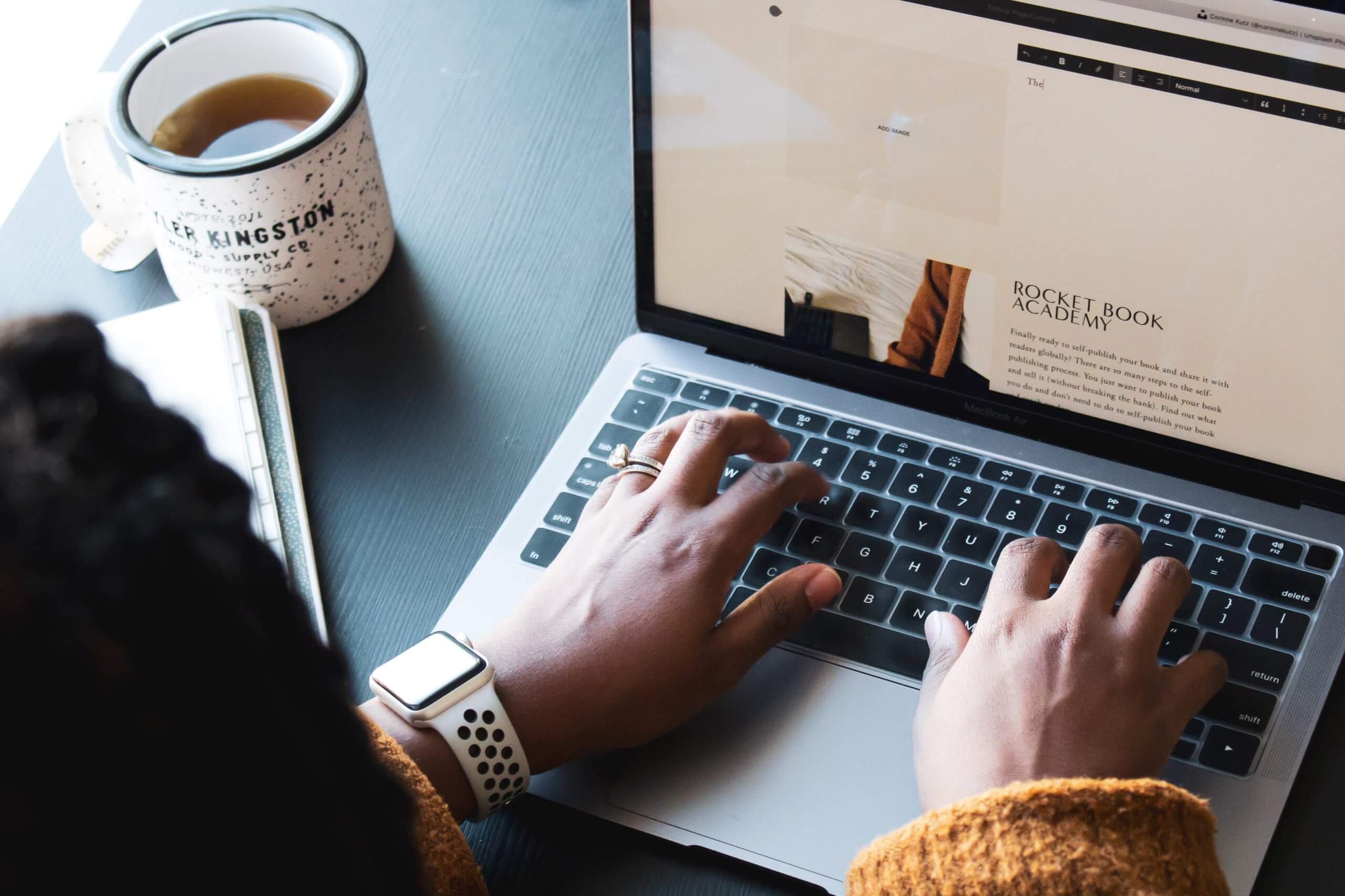 A woman typing on laptop with cup beside it