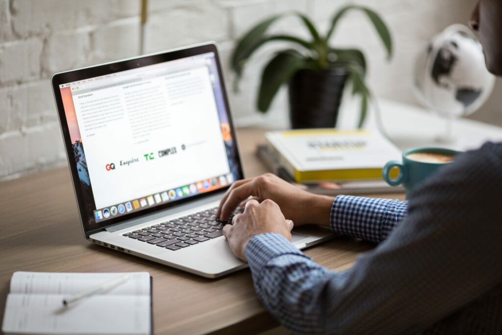 Hands typing on a laptop with cup of coffee and books on the side