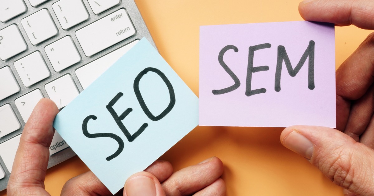 A person holding the word SEO and SEM on small papers over a keyboard