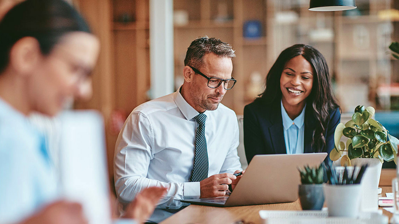 Three business professionals engaged in discussion at a table, each using a laptop for collaboration and productivity
